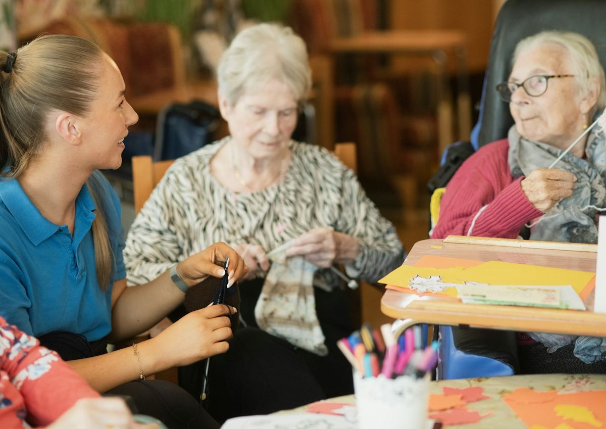 A caregiver helping two older women with a knitting project